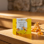 Natural Soap Cube – Crystal Amber 100 g on a honey-toned wooden vanity with pieces of amber